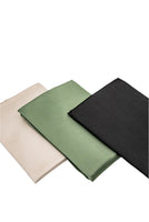 Three Sagrada BioSkincare Sagrada Mulberry Silk Pillowcases, in beige, green, and black 22-momme silk with thermoregulating properties, are neatly folded and arranged side by side on a white background.