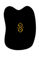 The Sagrada Gua Sha Nephrite Jade by Sagrada BioSkincare is a black, irregularly shaped tool with a gold decorative symbol, inspired by Traditional Chinese Medicine and designed to sculpt, detoxify, and revitalize your skin.