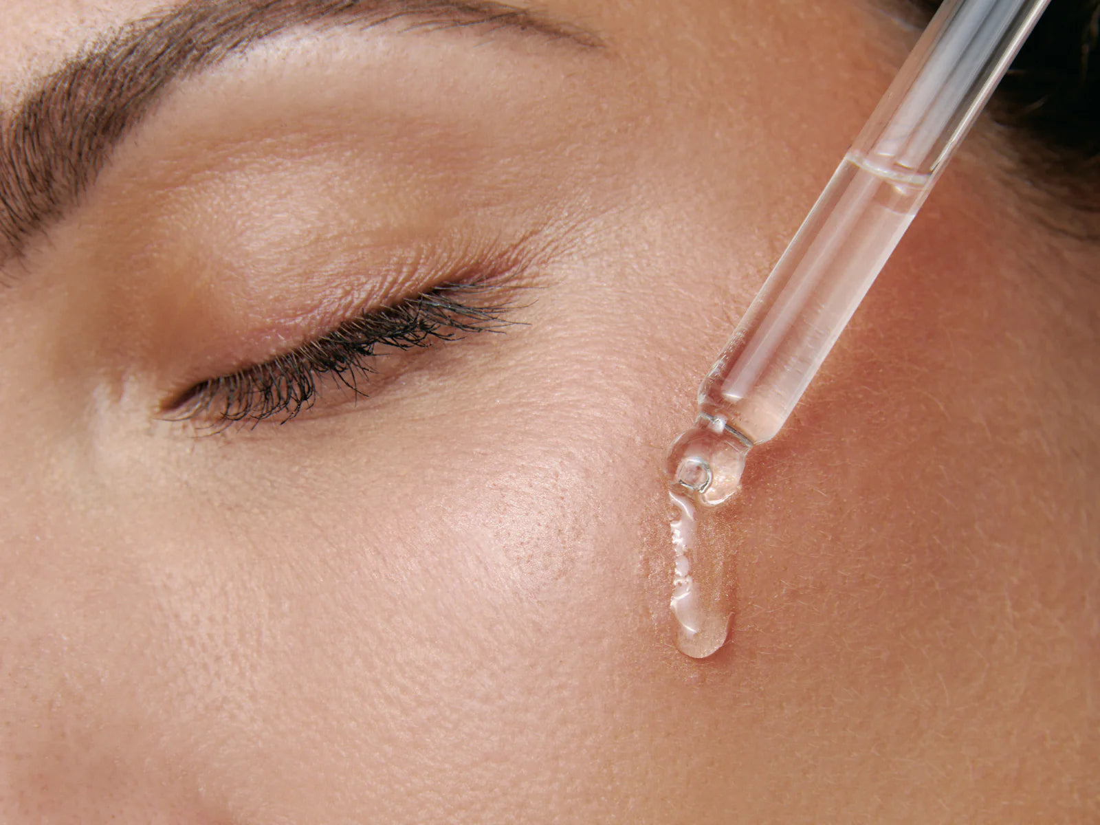 A close-up of a face with closed eyes as a dropper applies Adverto Beauty’s UNICLIFTING+ Intensive Firming & Tightening Serum to the cheek, highlighting smooth, hydrated, and healthy skin.