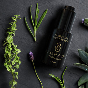 A 30 ml black bottle of Sagrada BioSkincare's Night Bakuchiol Serum – Gentle Alternative To Retinol rests on a dark surface, with fresh green herbs and lavender sprigs nearby. Gold text highlights its potent botanical blend.