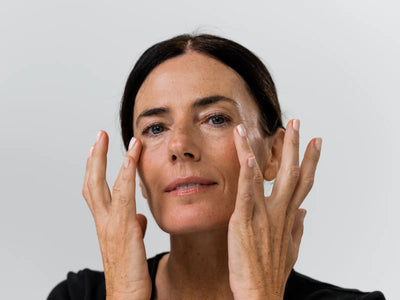 A dark-haired woman touches the skin under her eyes with both hands, appearing to apply Adverto Beauty’s UNICEYES Triple Action Eye & Lip Contour—an anti-wrinkle, anti-dark circles, and anti-puffiness product—against a plain light background.