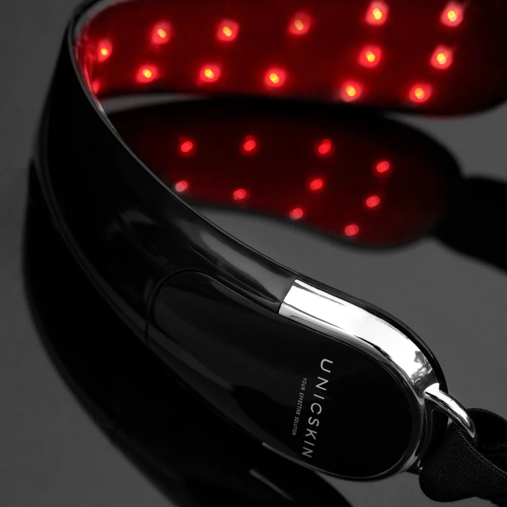 A close-up of the Unic Skin UNICLED Neck & Chin Device, featuring glowing red LED lights for skin firming and tightening, is shown on a glossy black surface.