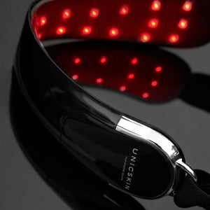 A close-up of the Unic Skin UNICLED Neck & Chin Device, featuring glowing red LED lights for skin firming and tightening, is shown on a glossy black surface.