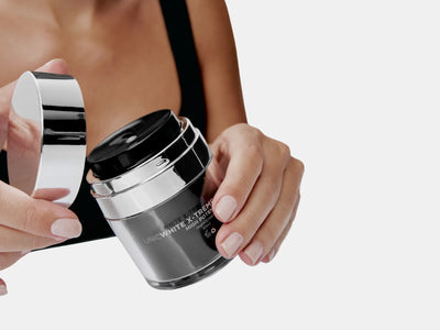 A person with manicured nails opens a jar of Adverto Beauty’s UNICWHITE X-TREME Complex—an effective night cream formulated to reduce dark spots—against a plain white background.