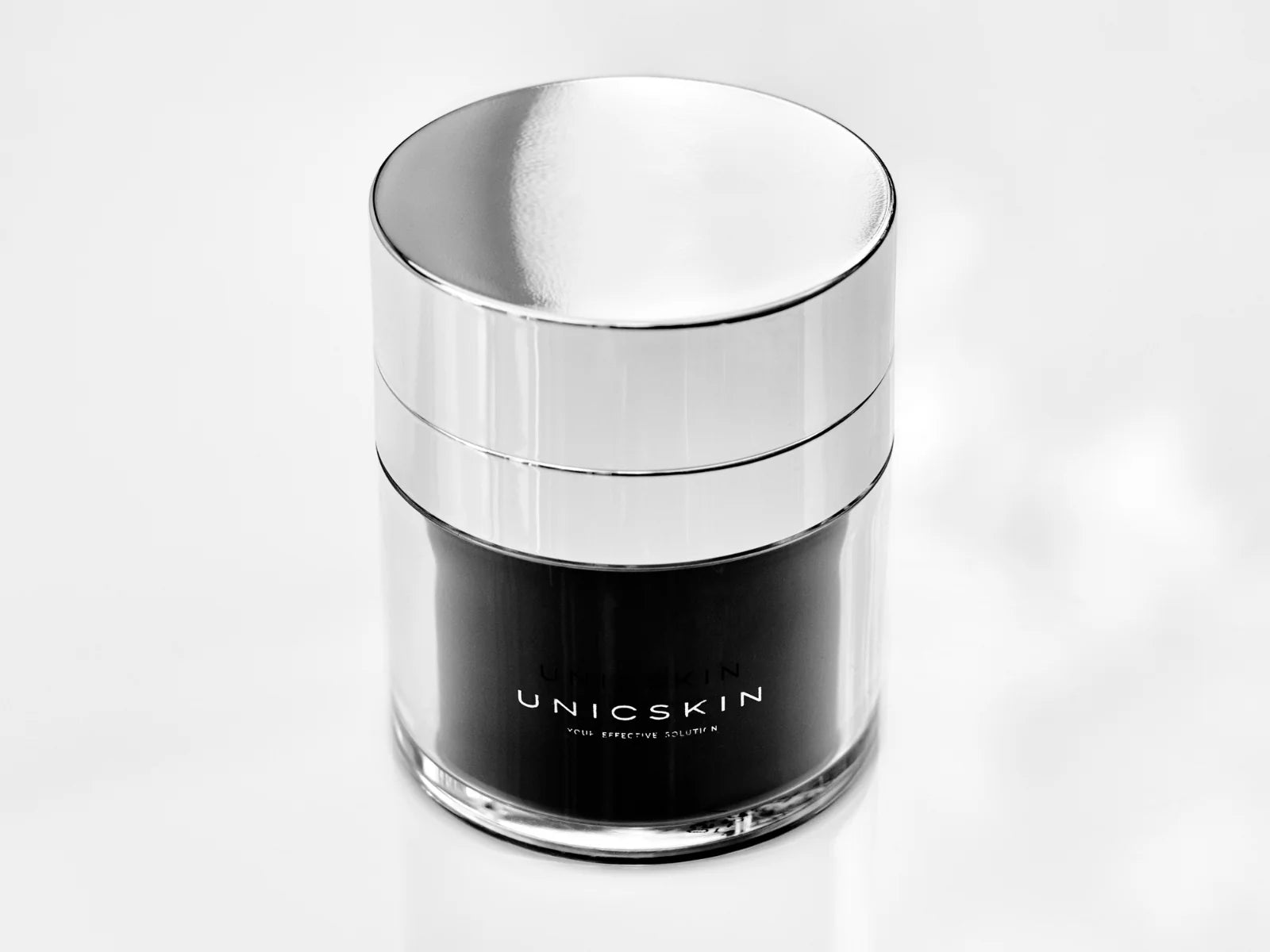 The UNICWHITE X-TREME Complex by Adverto Beauty—a sleek jar with a metallic lid and "UNICSKIN" label—sits on a glossy white surface, ideal for targeting dark spots and uneven skin tone overnight.