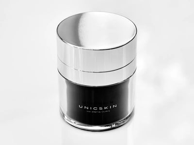 The UNICWHITE X-TREME Complex by Adverto Beauty—a sleek jar with a metallic lid and "UNICSKIN" label—sits on a glossy white surface, ideal for targeting dark spots and uneven skin tone overnight.