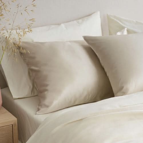 A cozy bed features Sagrada BioSkincare's Sagrada Mulberry Silk Pillowcase—cream-colored, 22-momme silk that pampers your skin and hair while providing natural thermoregulation for comfortable sleep year-round.